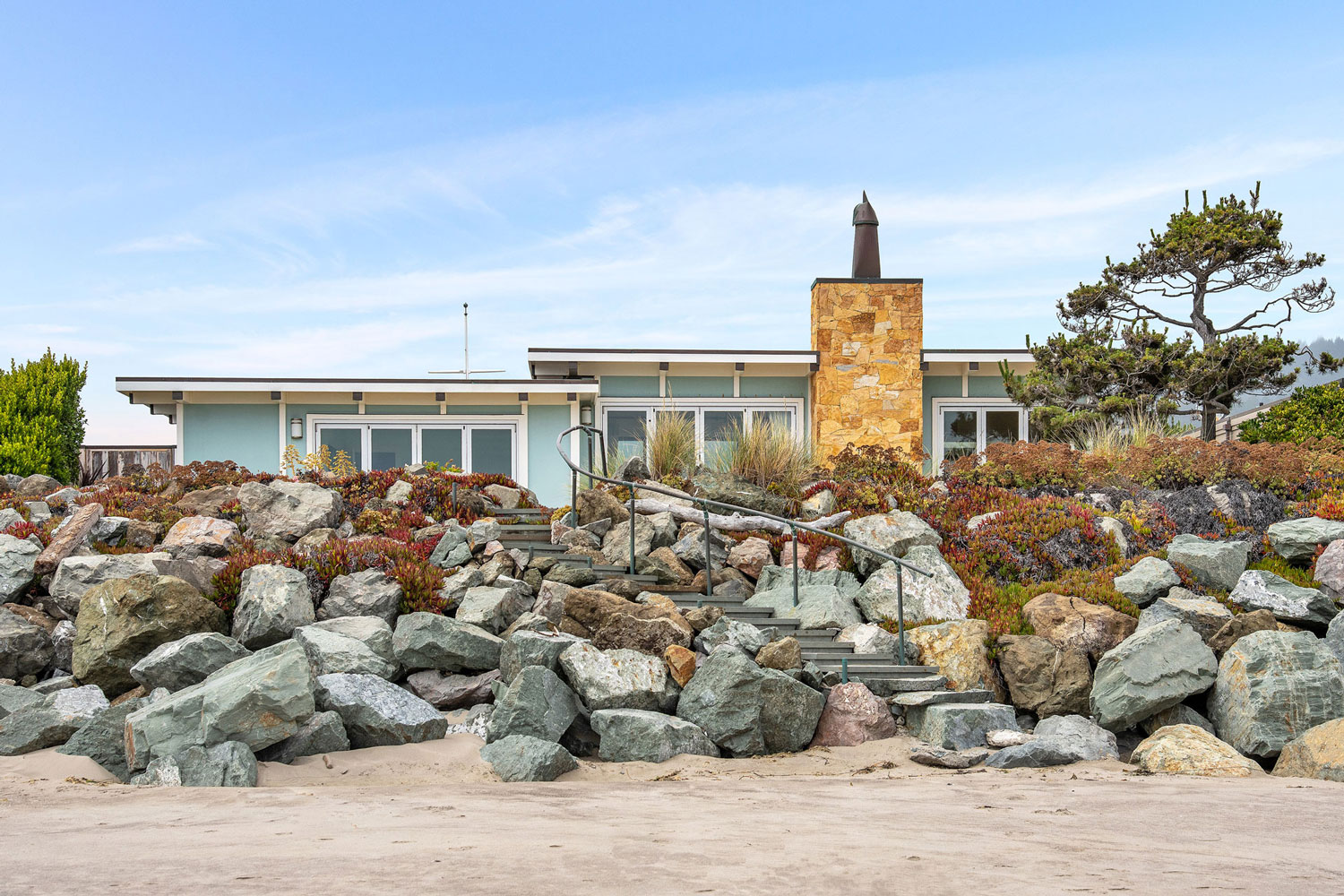 Oceanfront home in Stinson Beach. Fully renovated house with custom built steps leading to a private beach. Exterior painted aqua marine blue with white trim.