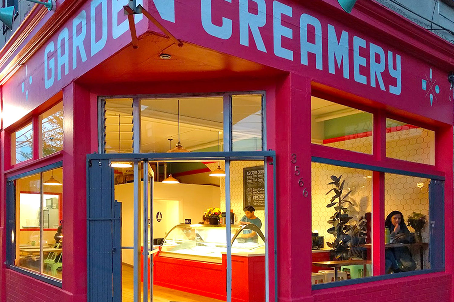 Ice cream shop. Exterior painted bright red. Large windows. Interior has custom lighting, countertops, and white tiled walls.